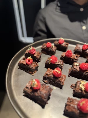 Tray of gourmet chocolate brownie bites topped with fresh raspberries and edible gold, served as a luxury catering dessert.