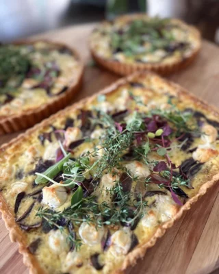 Freshly baked chicken, cheese and caramelised onion tart garnished with herbs, served as part of a catering menu.