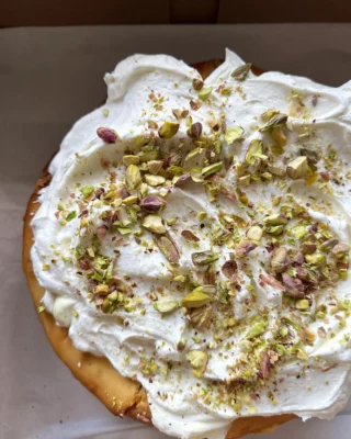 Homemade pistachio cheesecake topped with whipped cream and crushed pistachios, perfect for dessert catering and events.